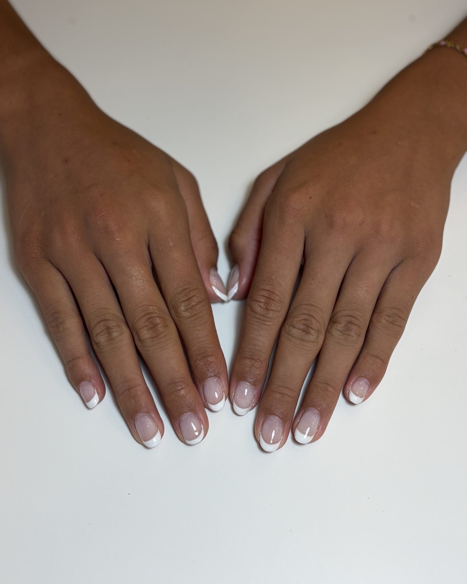 Two hands resting on a white table, wearing a clean white French tip on short, squared natural nails.